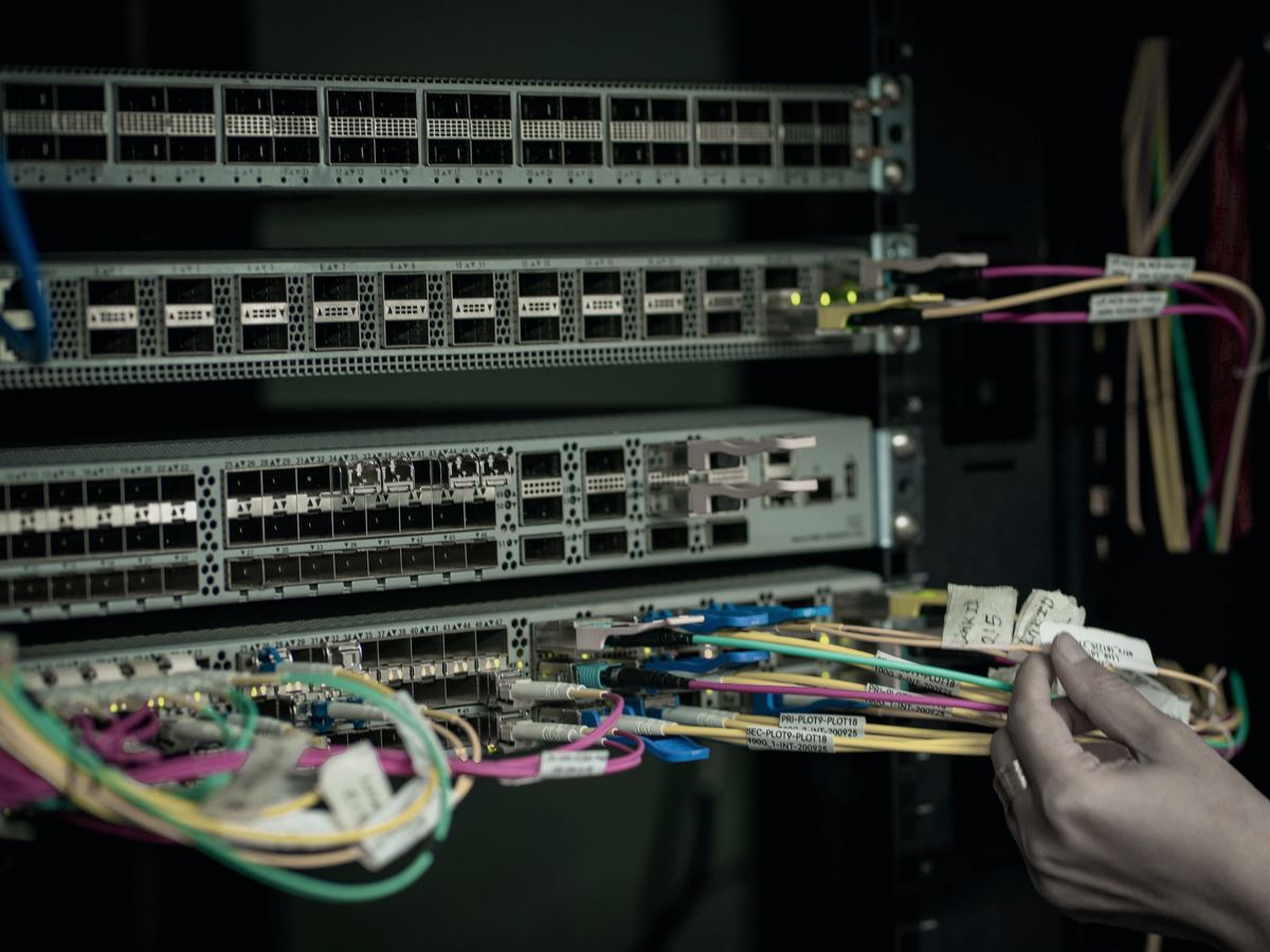 Techniker steckt beschriftete Glasfaser-Patchkabel in einen Switch